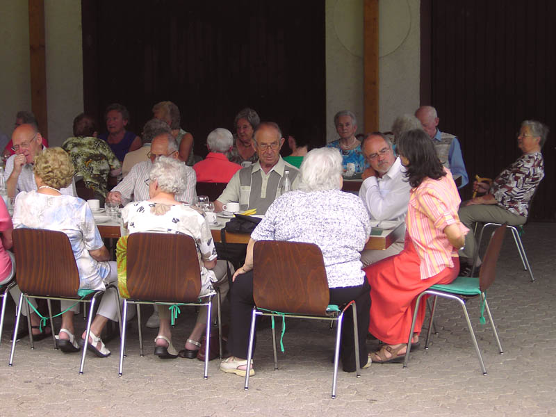 Bild vom Seniorenkaffee unter der Überdachung am Feuerwehrgerätehaus, die Organisatorin unterhält sich mit Pfarrer Löhde